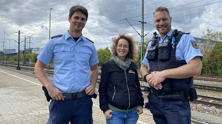 Eine Frau steht zwischen zwei Polizisten am Bahngleis.