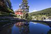 Ausblick auf eine rote Kapelle, einem Teich und grünen Wälder im Hintergrund.