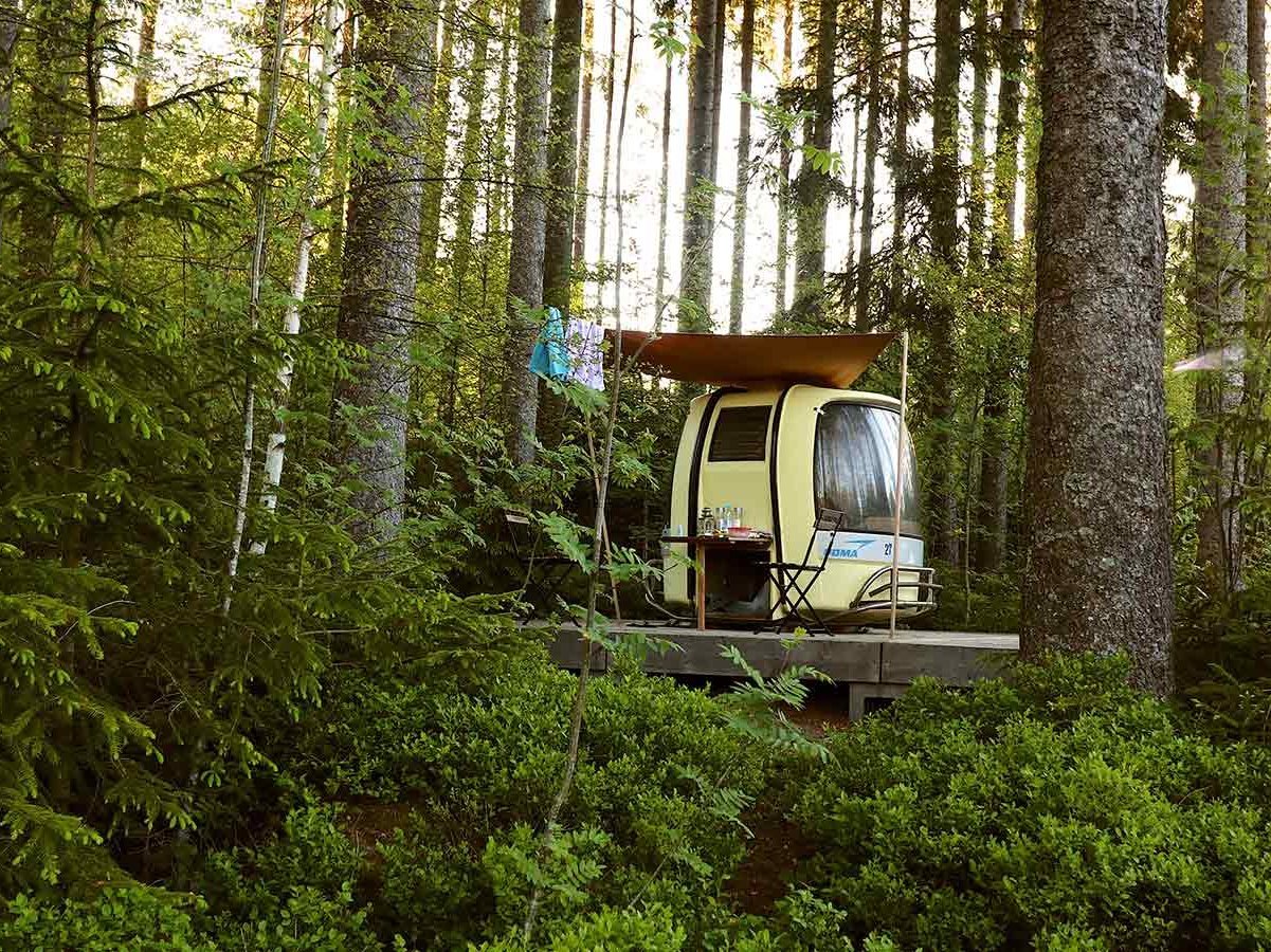 Mitten im Wald steht ein kleiner Camper auf einer Holzplattform.