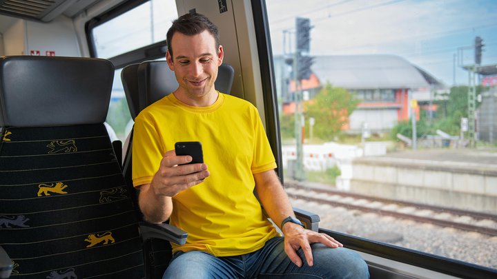 Ein Mann sitzt in einem bwegt-Zug und schaut auf sein Smartphone