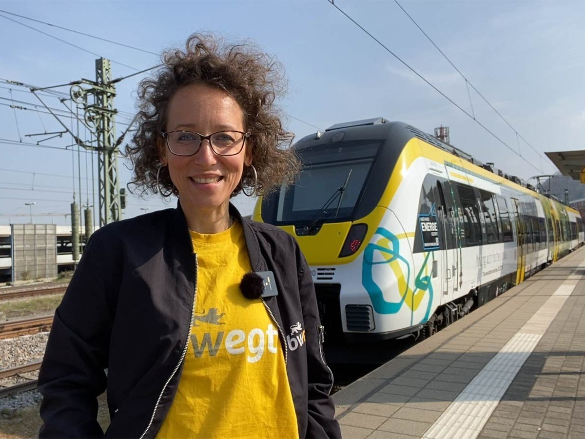 Frau steht am Bahnsteig vor einem Batteriezug.