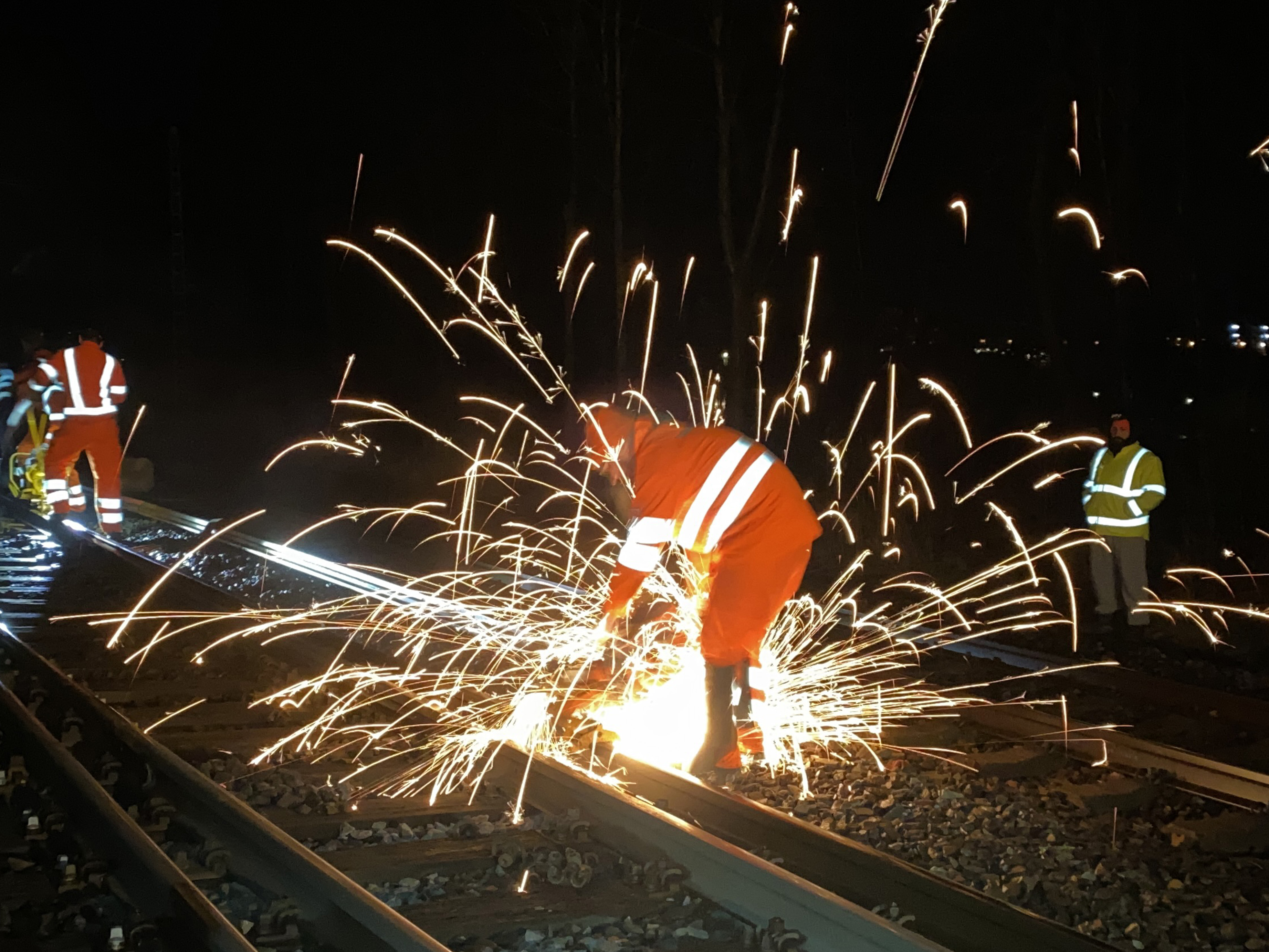 Funken sprühen beim Schweißen von Gleisen auf einer Baustelle bei Nacht.