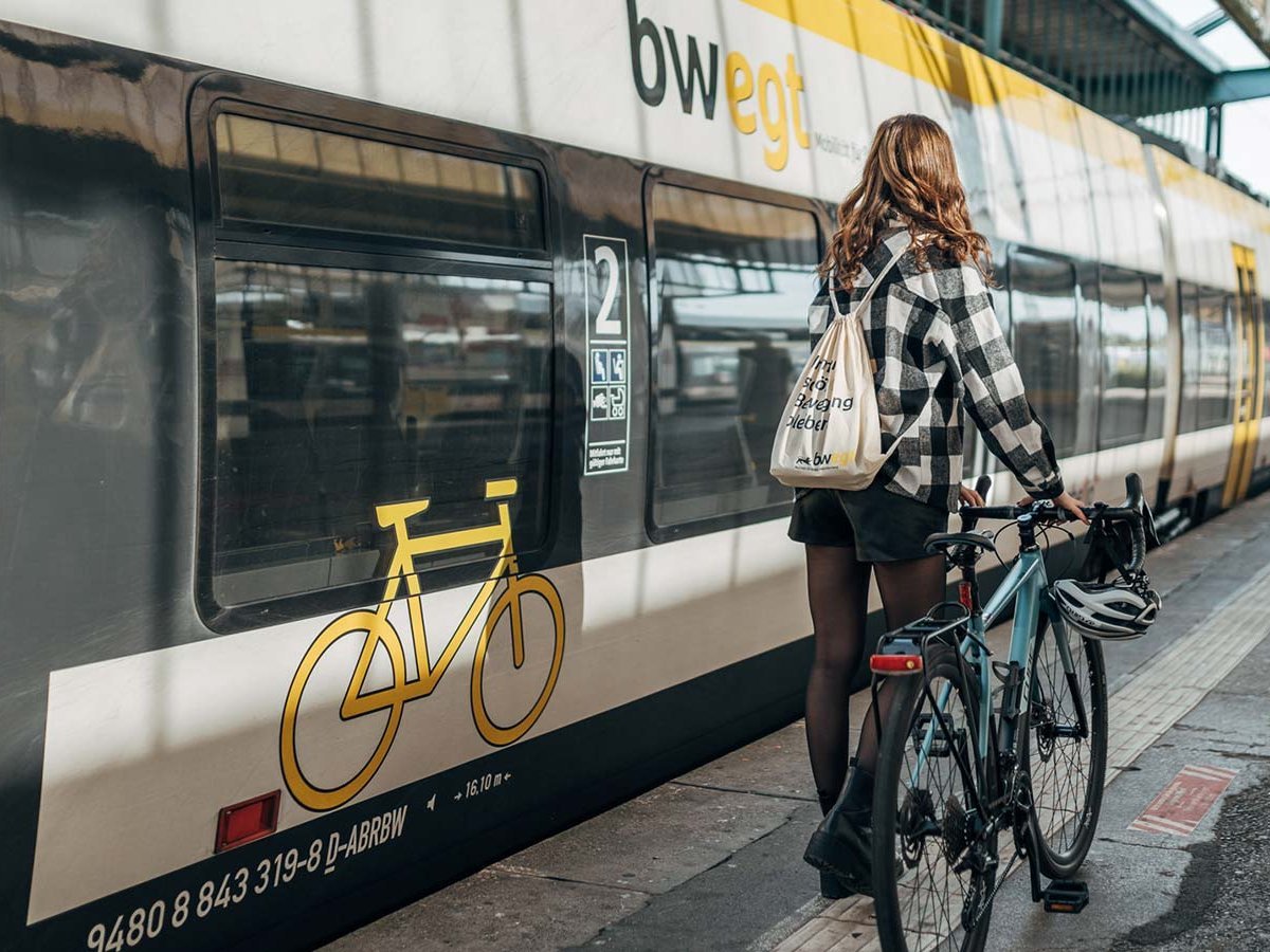 Junge Frau läuft mit ihrem Fahrrad am Bahnsteig zu einer Bahn.