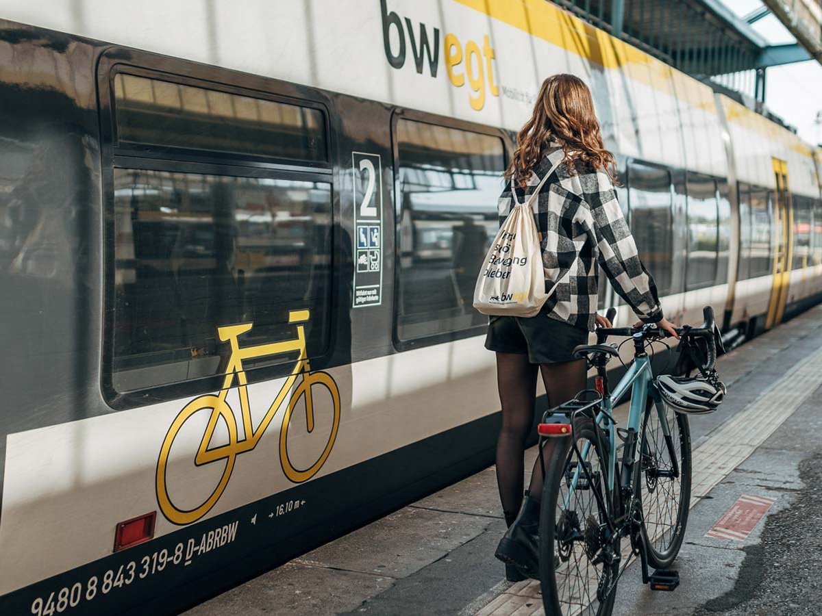 Junge Frau geht mit Fahrrad den Bahnsteig entlang. 