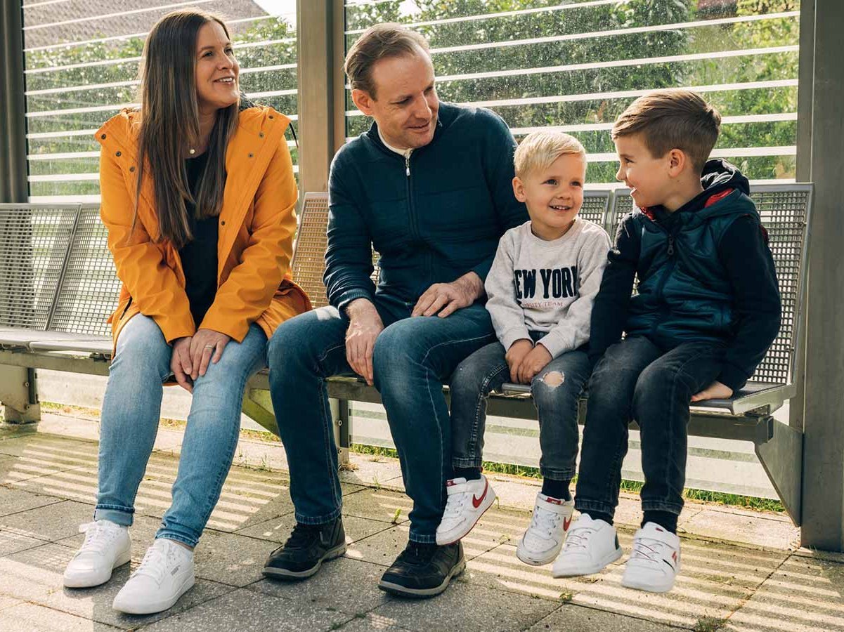 Familie mit zwei Kindern sitzt am Bahnsteig auf einer Bank.