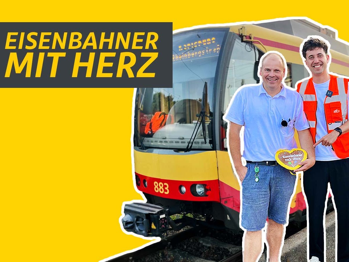 Lokführer steht neben Mann in Warnweste vor einer Straßenbahn.