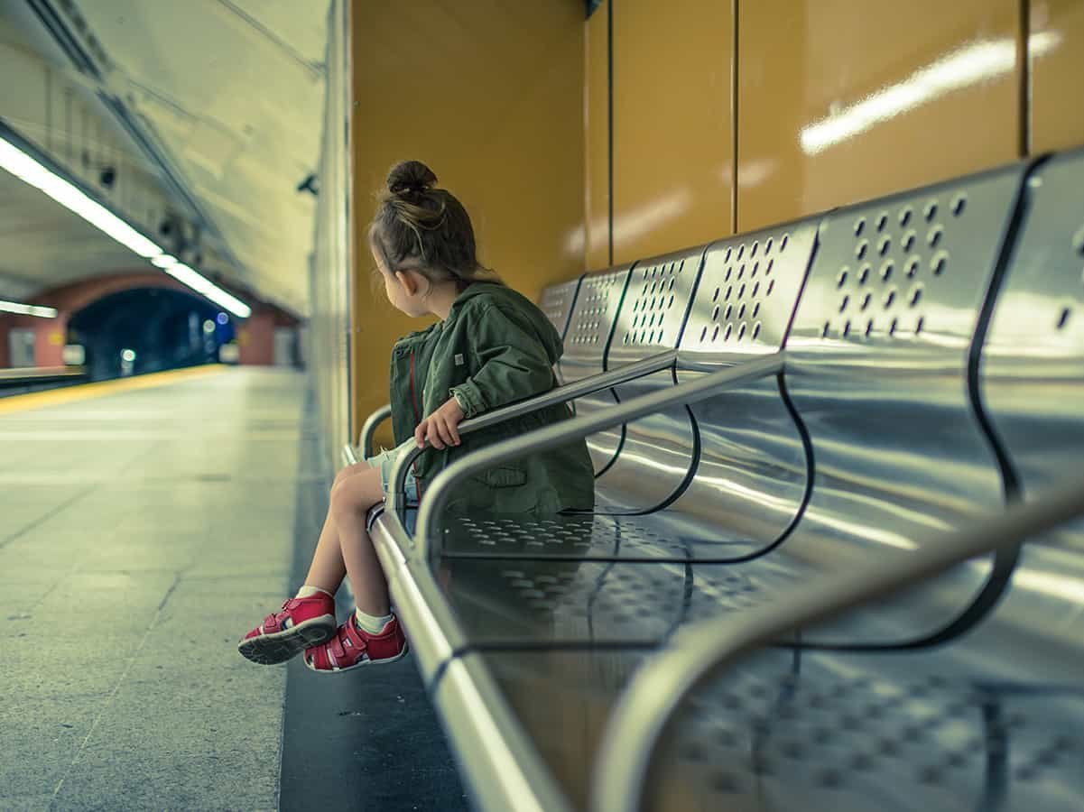 Junges Mädchen sitzt alleine auf einer Bank am Bahnhof.