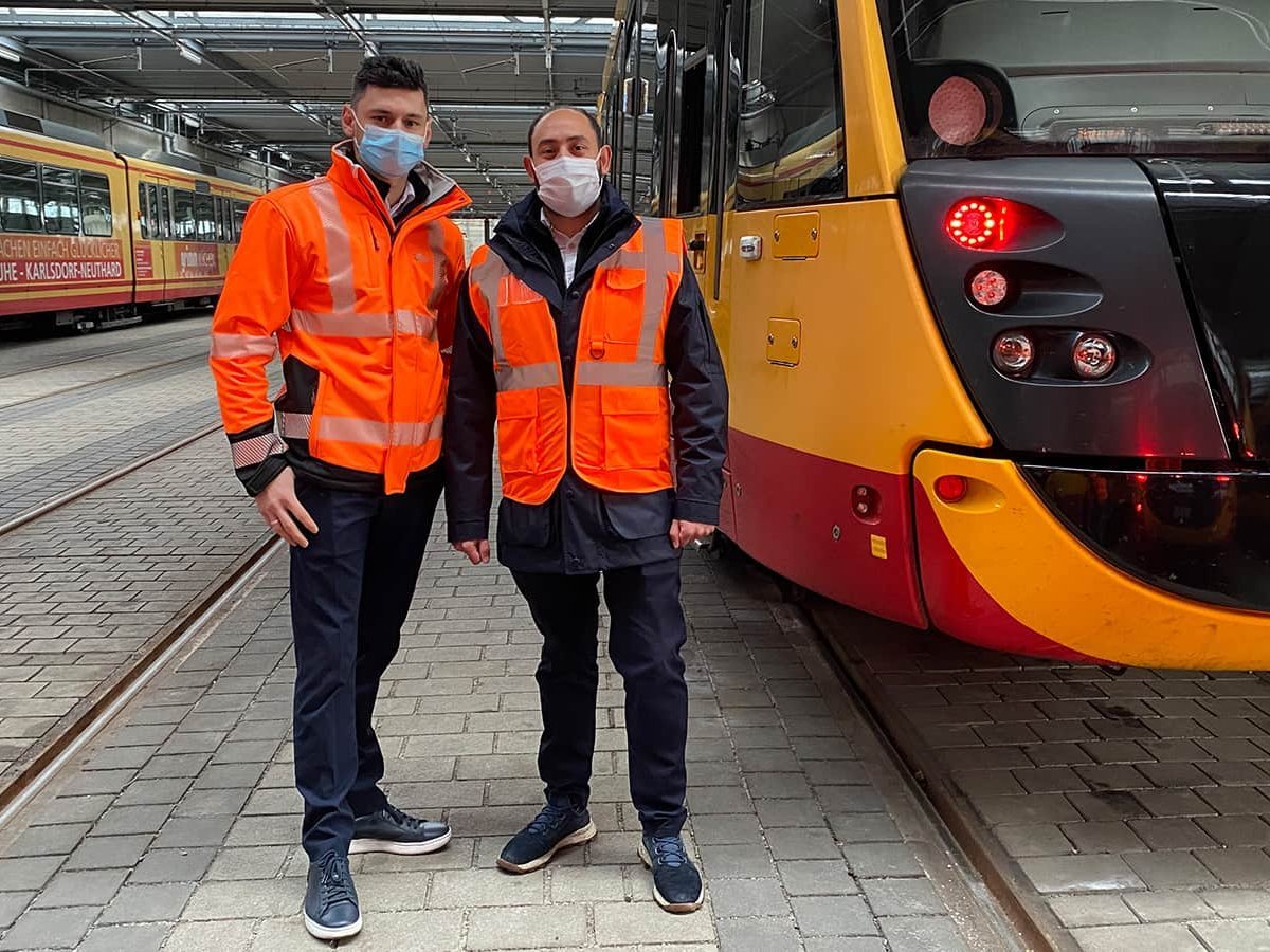 Zwei Lokführer mit Migrationshintergrund stehen neben einer Straßenbahn.