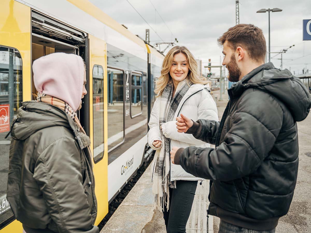 Drei junge Menschen reden am Bahnsteig.