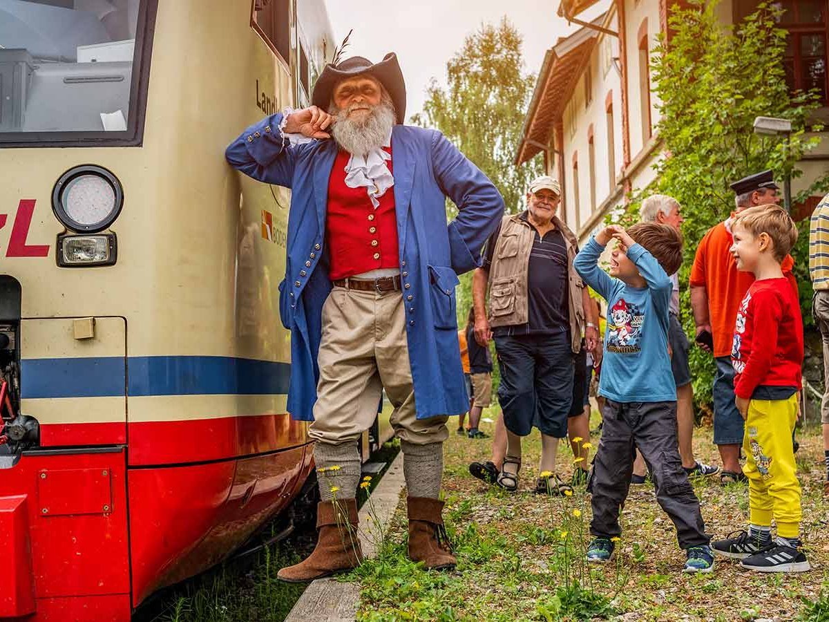 Mann im Räuber-Kostüm lehnt an einer Bahn. Um ihn herum stehen Kinder.