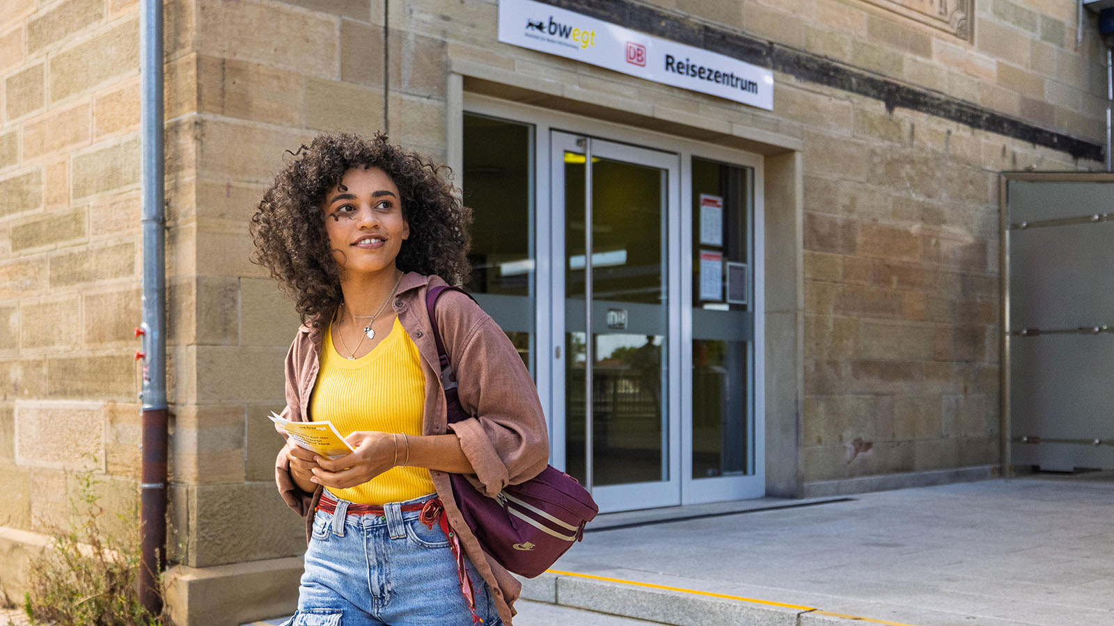 Eine junge Frau verlässt das Reisezentrum mit einem Flyer in der Hand