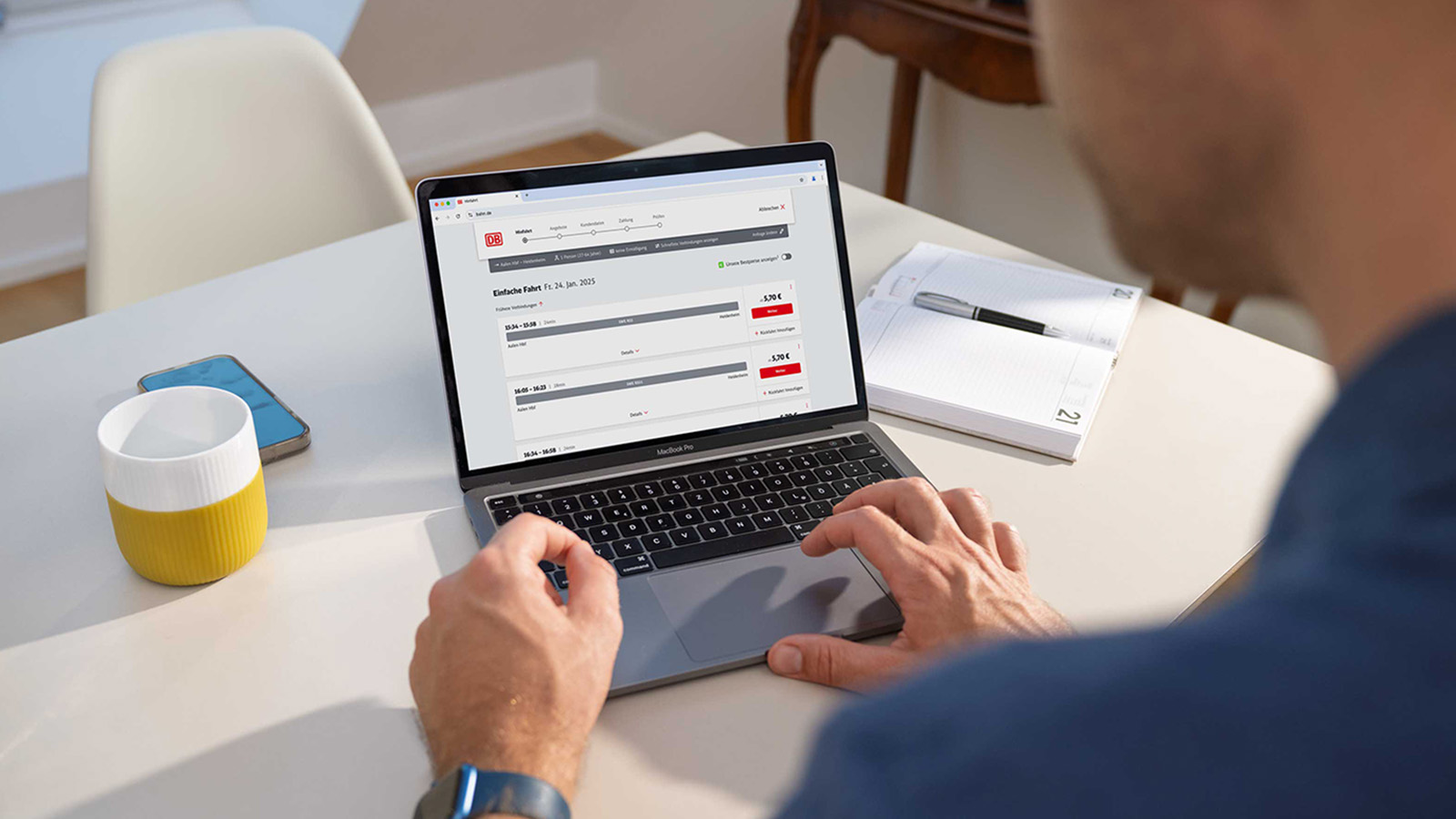 POV-Sicht auf einen Laptop mit der DB-Fahrplanauskunft und einer tippenden Hand auf dem Touch-Pad