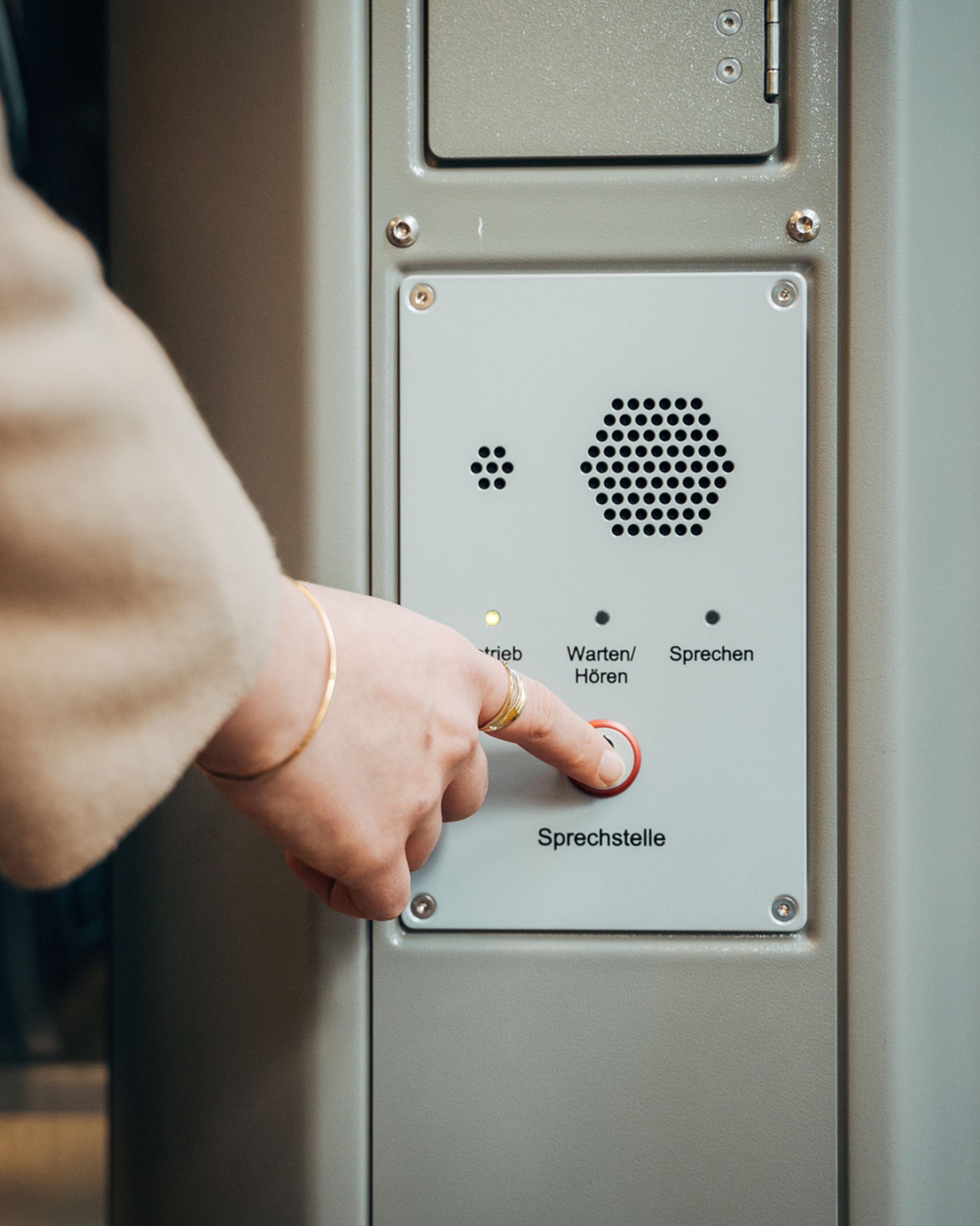 Finger einer Person drückt auf die Notruftaste an der Sprechstelle im Zug.