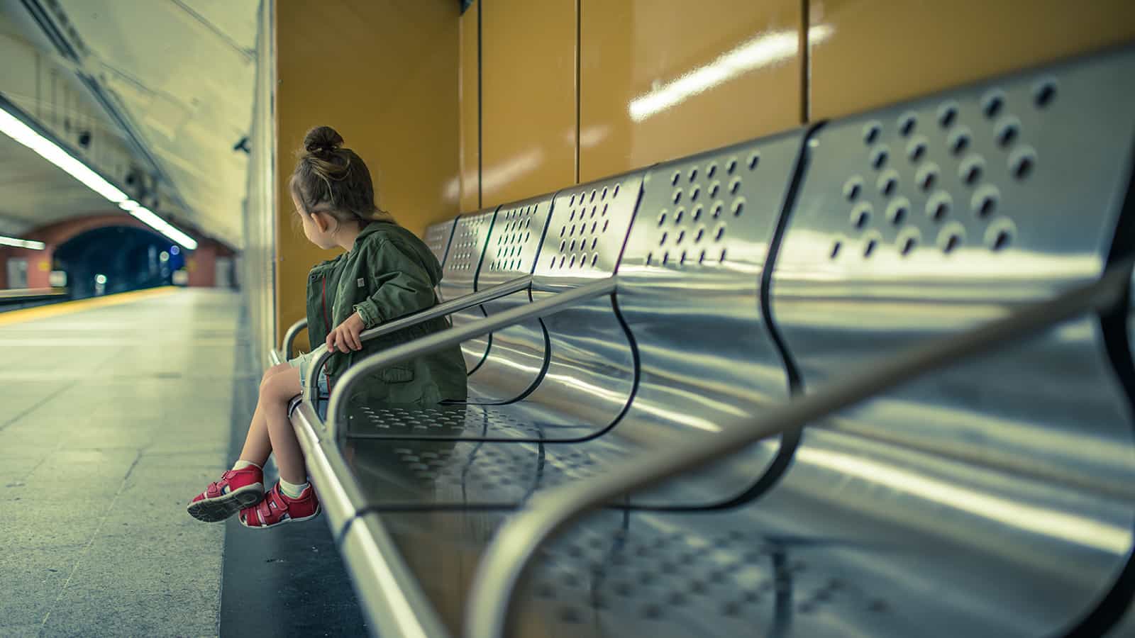 Junges Mädchen sitzt alleine auf einer Bank an einer verlassenen Bahnhaltestelle.