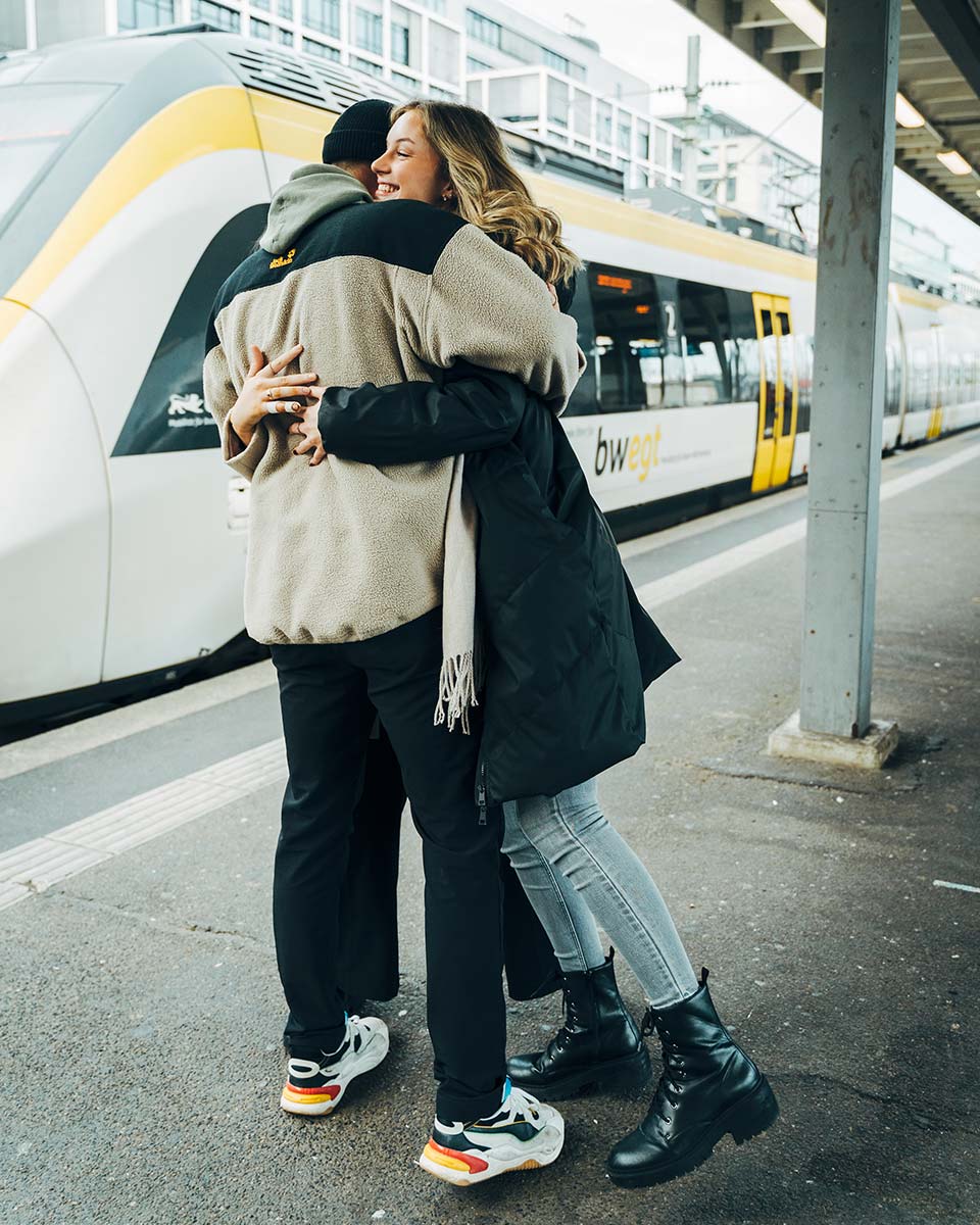 Junge Frau und Mann umarmen sich am Bahngleis.