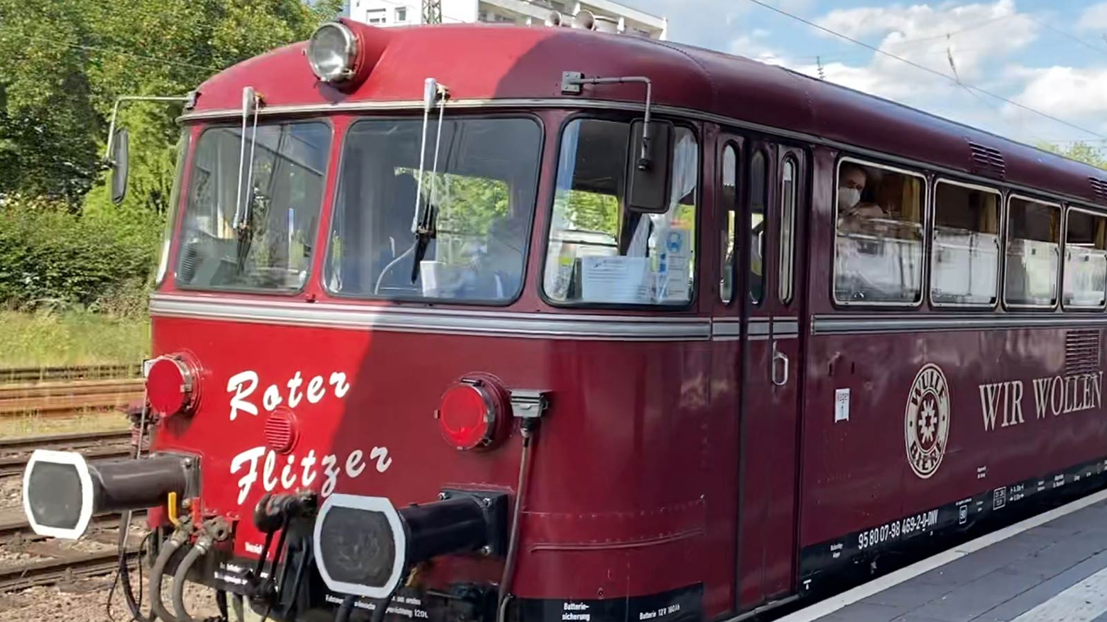 Historische Bahn in dunkelroter Farbe steht am Bahngleis.