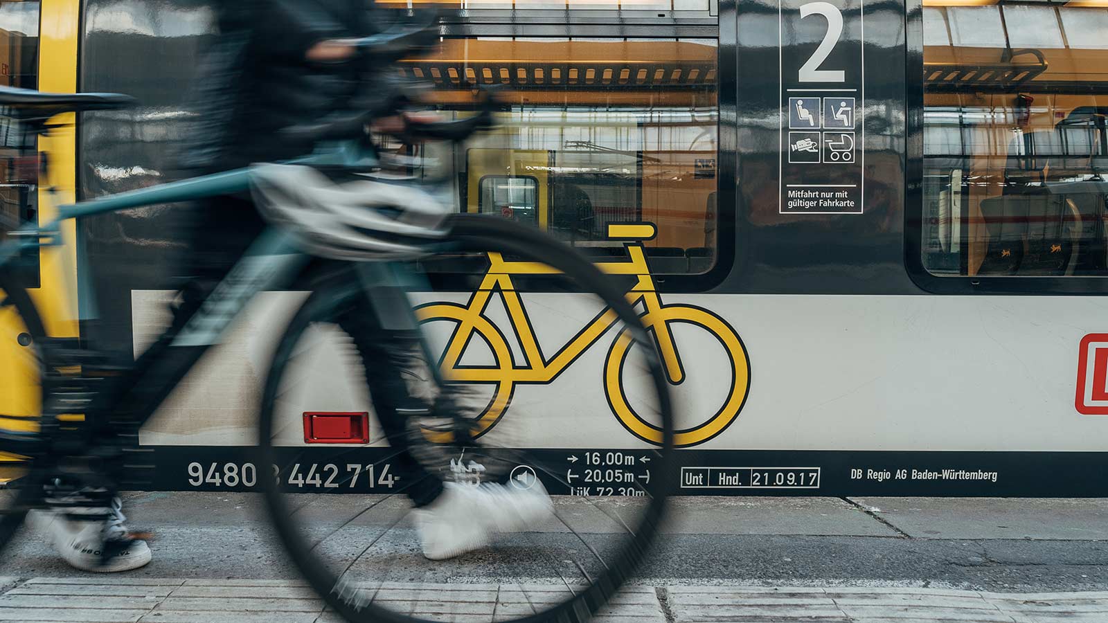 Fahrrad wird an Bahn mit Fahrradlogo vorbeigerollt