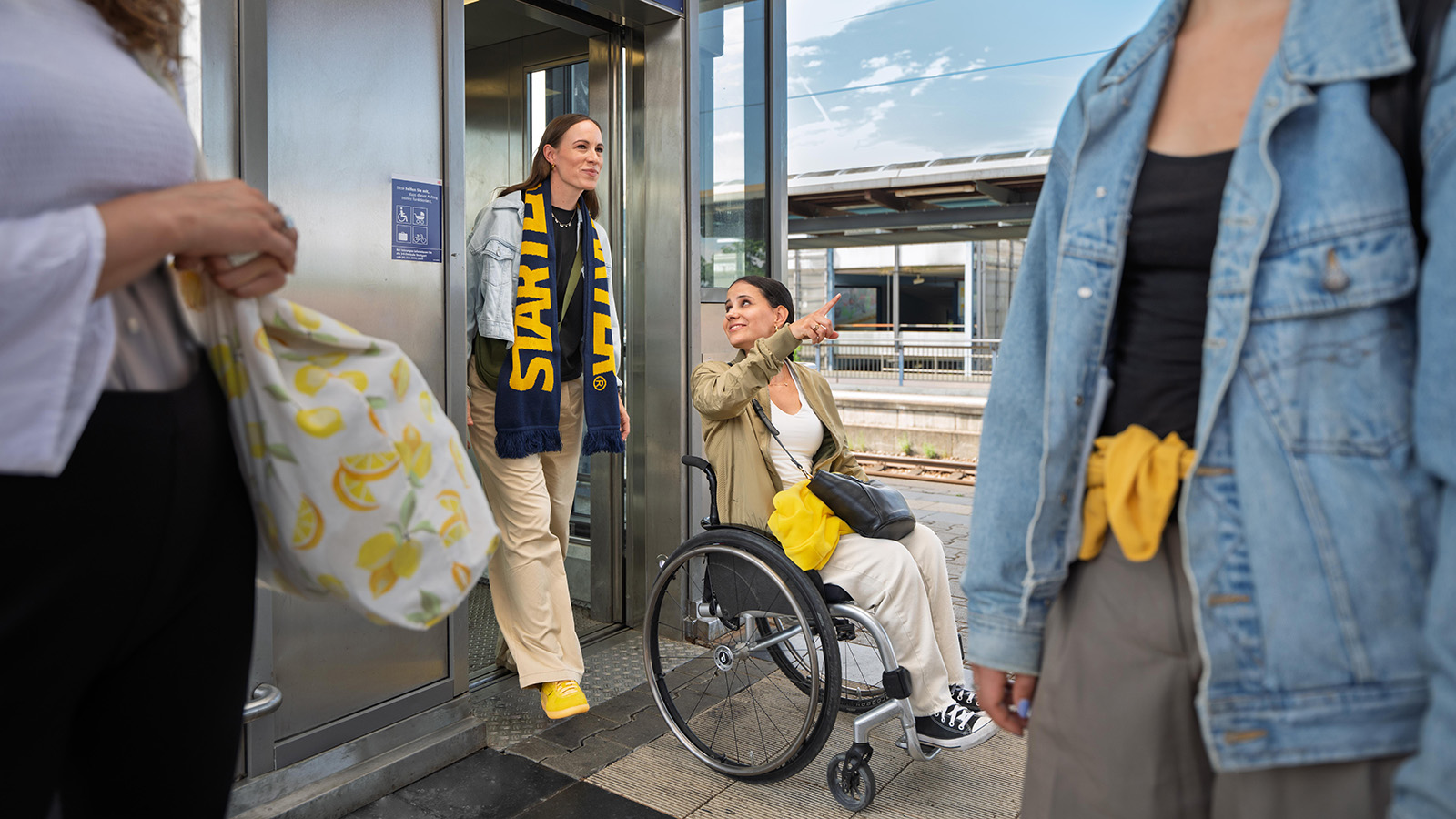 Eine Frau und eine Frau im Rollstuhl steigen aus einem Aufzug an einem Bahnsteig aus