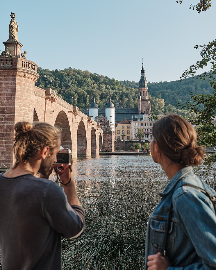 Ein junges Paar macht ein Foto von der Alten Brücke in Heidelberg